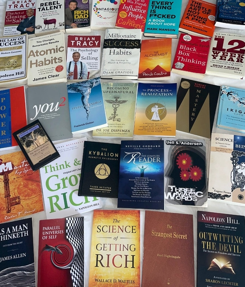 Multiple rows of various metaphysical, esoteric, business, and self-help books laid out on a bed including Think and Grow Rich, Neville Goddard's Complete Reader, The Kybalion, The Psychology of Selling, Three Magic Words, Atomic Habits, Millionaire Success Habits, How To Win Friends and Influence People, Rich Dad Poor Dad, and many more.